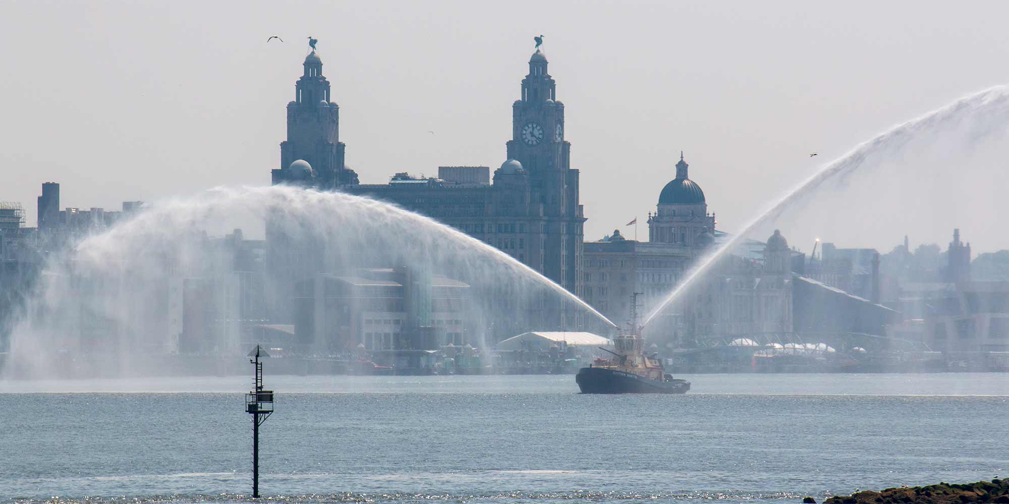 Tugboat spraying water on the River Mersey in front of the Liver Buildings